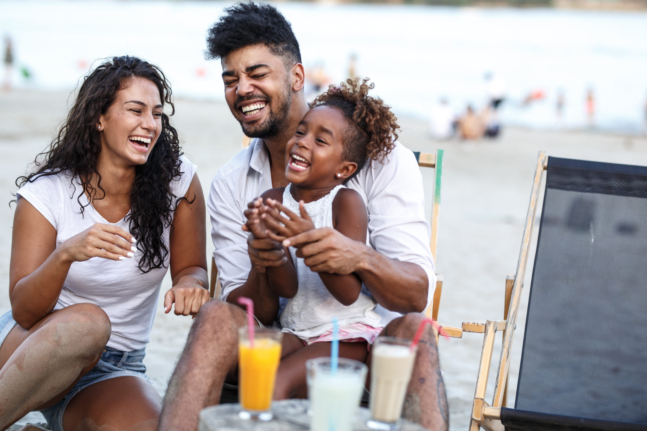 a young family sitting on a beach and laughing