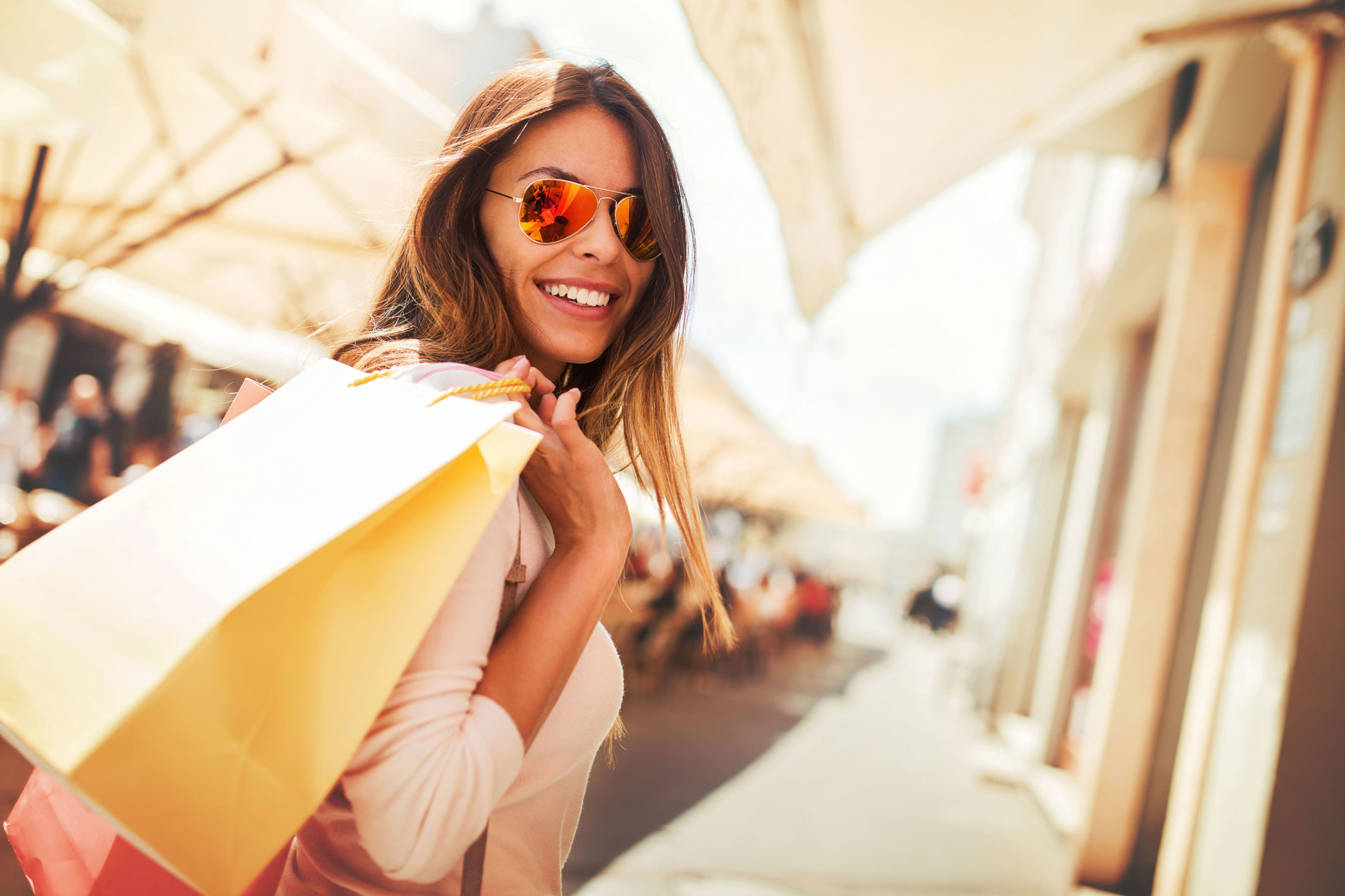 a smiling woman with sunglasses on with shopping bags over her shoulder