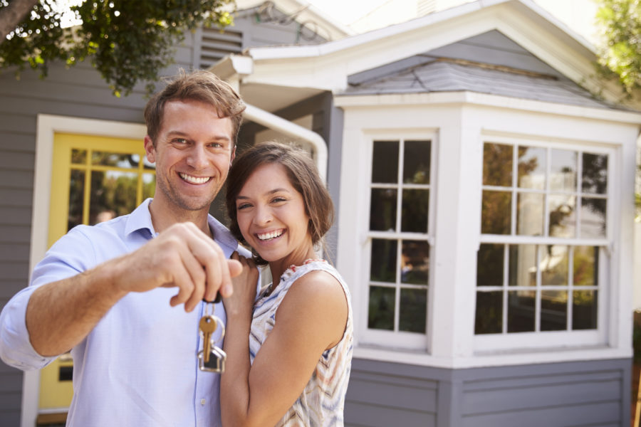 a young couple smiling in front of a house and holding out house keys