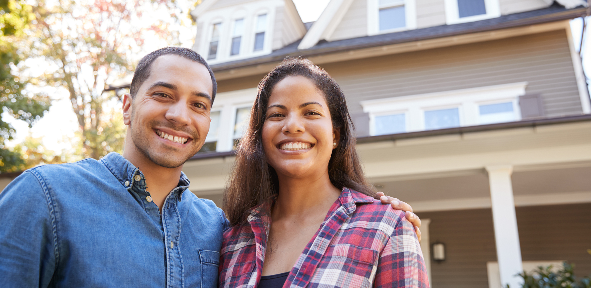 young couple smiling in front of house