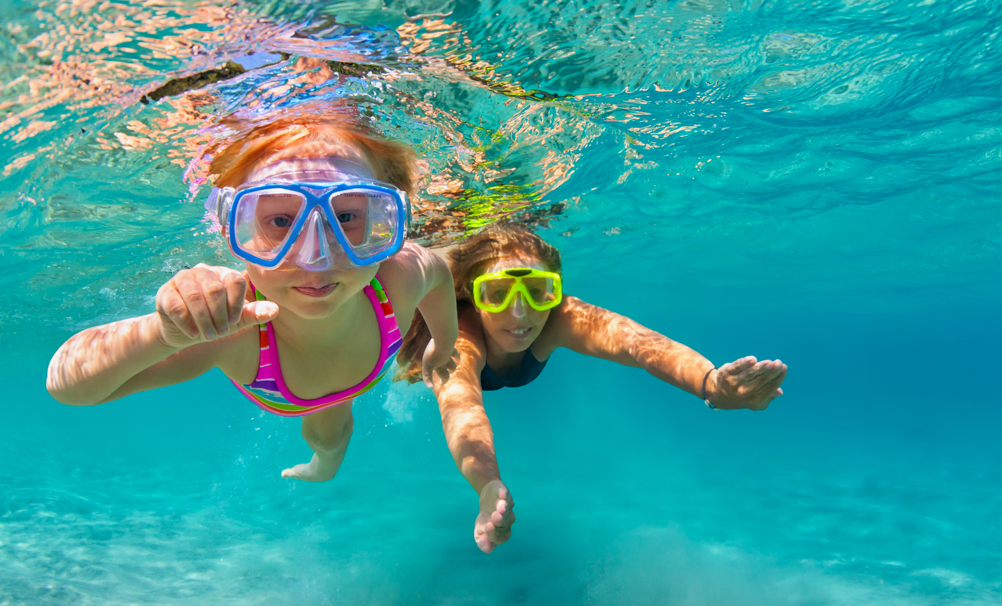 a mom and a daughter with goggles on swimming underwater