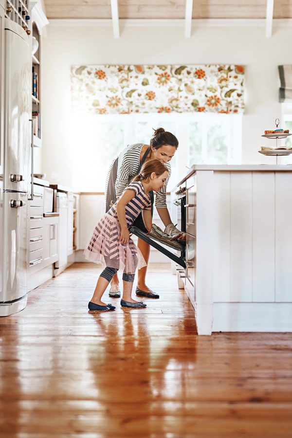Mother and young daughter in kitchen placing something in the oven