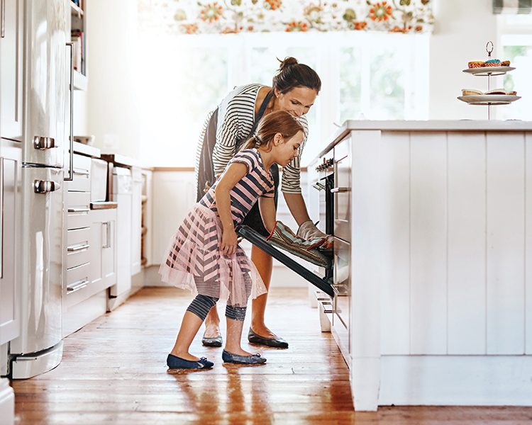 Mother and young daughter in kitchen placing something in the oven