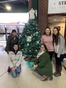 Women smiling in front of decorated Christmas tree in a baseball stadium