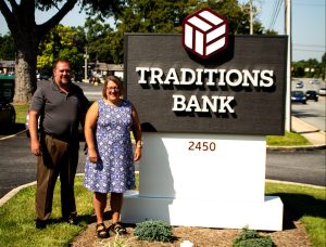 branch manager and customer in front of traditions bank sign