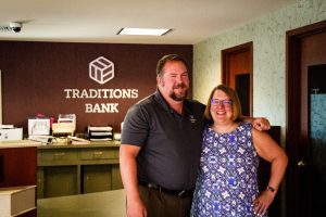 branch manager and client pose in front of traditions bank sign