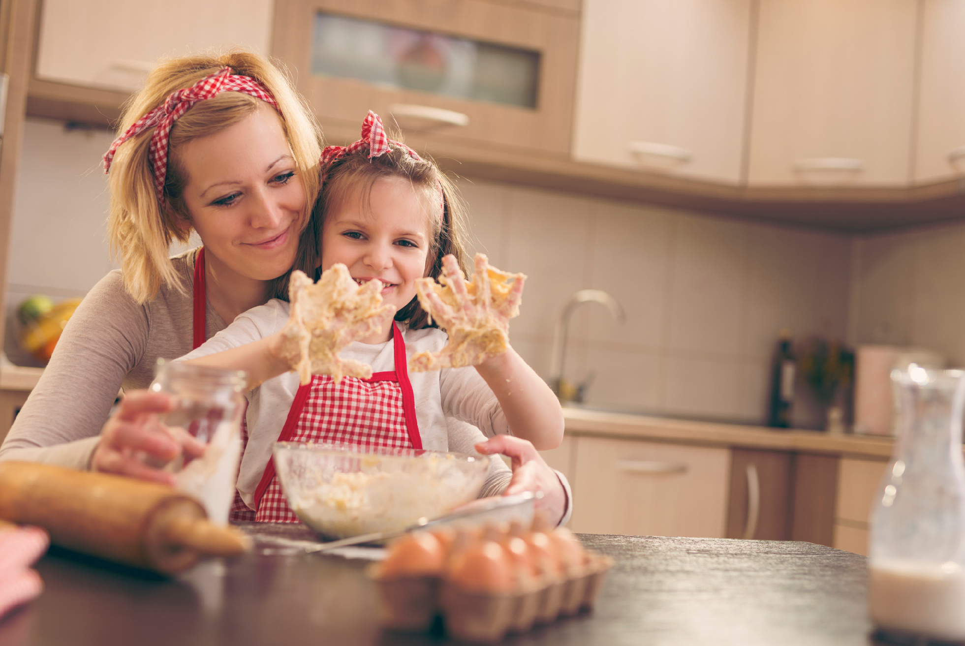 young girl and mom laughing at the little girl's messy hands while they bake food