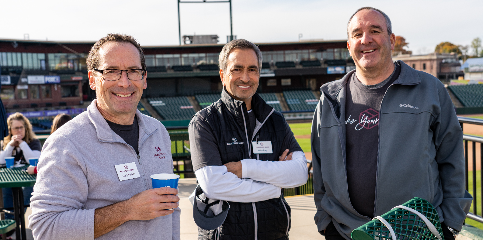 three men standing together smiling at an event in a baseball stadium