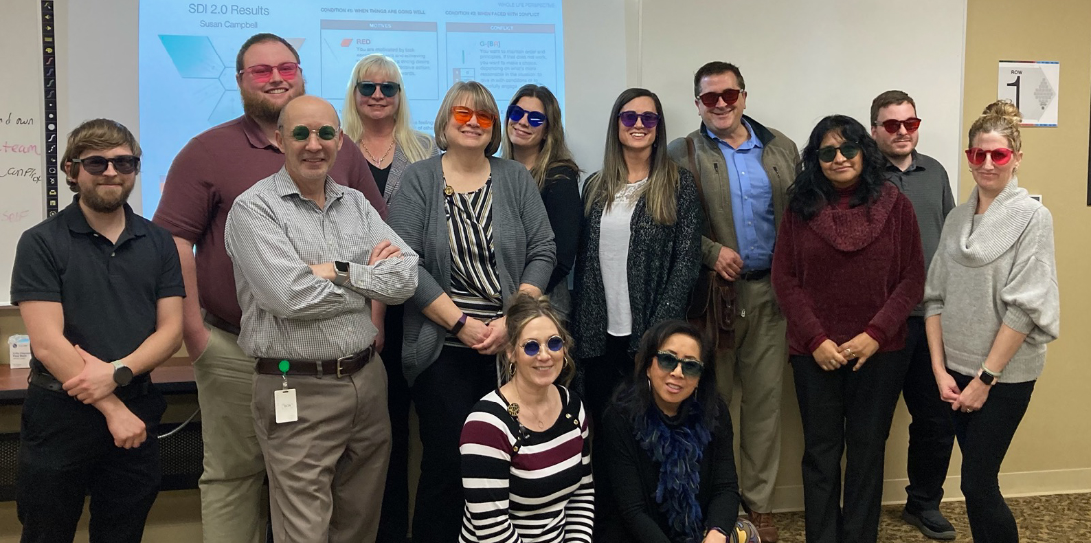 A group of male and female coworkers take a group photo wearing silly glasses following a training