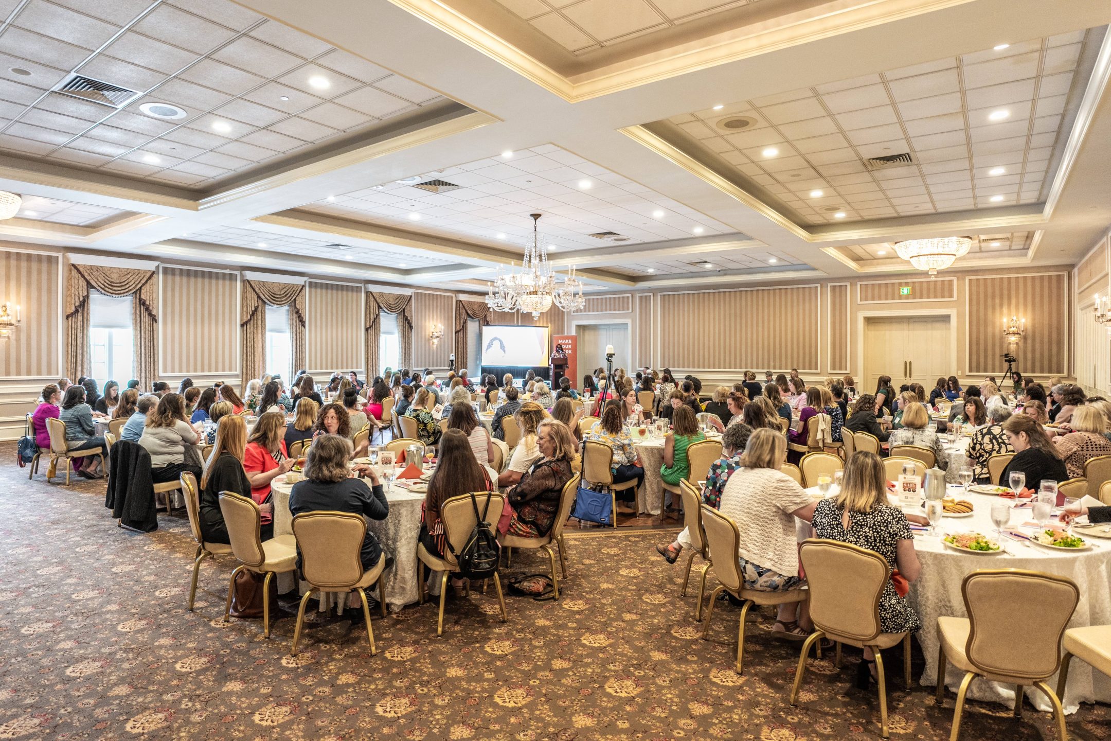 Wide shot of event attendees sitting at their tables in a large inside event space