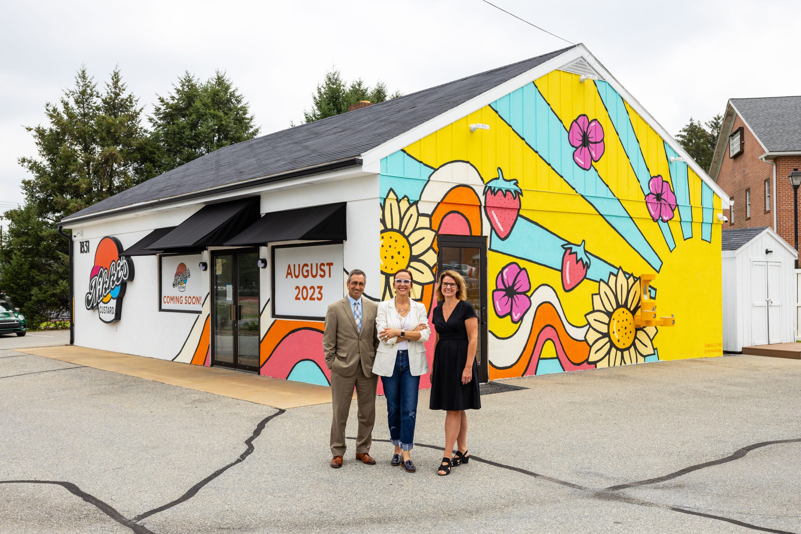 A man and two women smiling in front of a colorful custard shop